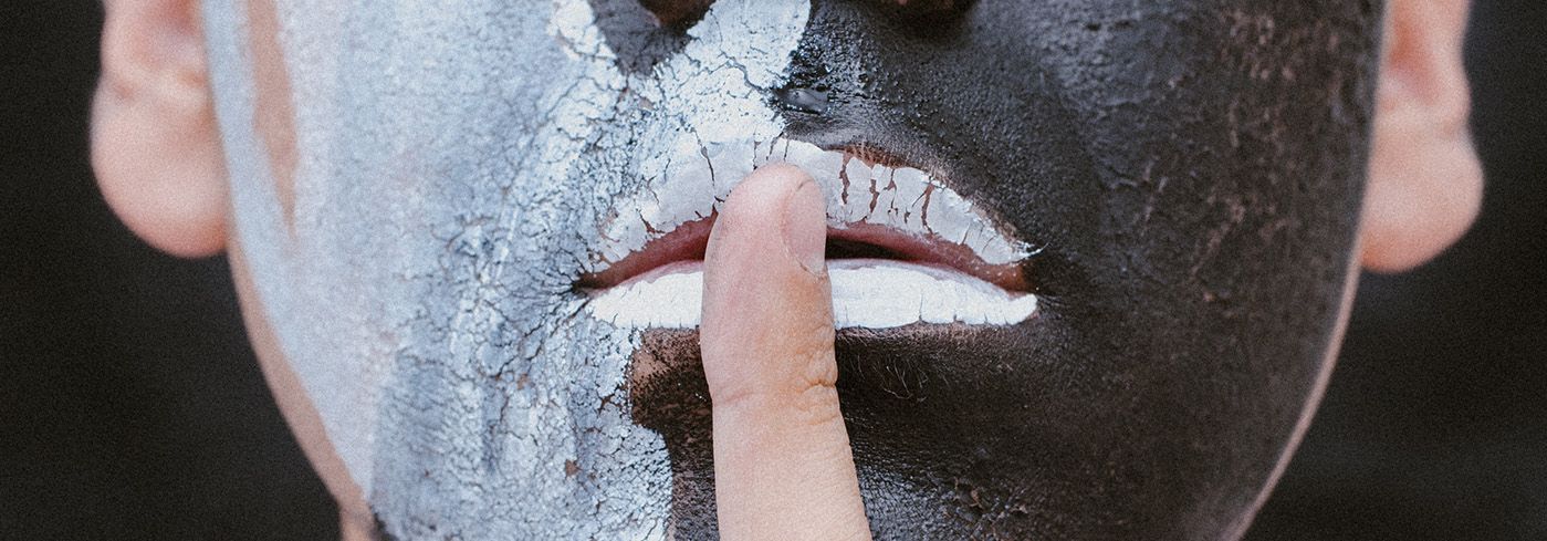 Bemaltes Gesicht mit Zeigefinger vor dem Mund